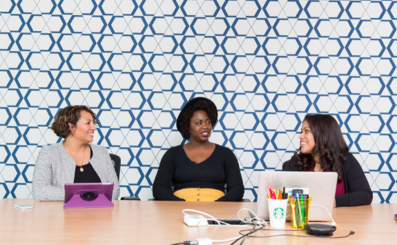 Three women sit around a boardroom table at work